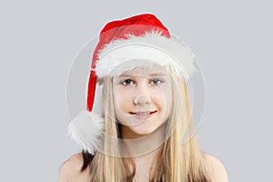 Christmas kid girl in red Santa hat smiling on gray background, closeup portrait