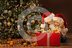 Christmas Kids with Big Red Gift Box full with Present Toys. Two Little Girls next to Xmas Tree Decorated with Lights Golden