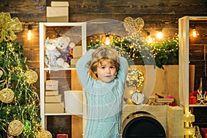 Christmas kids - happiness concept. Happy little child dressed in winter clothing think about Santa near Christmas tree