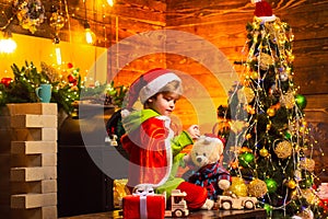 Christmas kids - happiness concept. Little Santa Claus gifting gift. Home Christmas atmosphere. Cheerful cute child