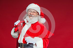 Christmas. Kind and tired Santa Claus in white gloves carries a red bag with gifts over his shoulder. Isolated on red