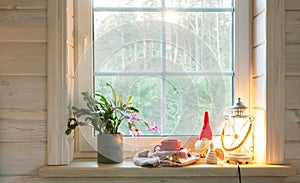Christmas lantern, Angel, Christmas gnome, Christmas Cactus and red mug on the window of a wooden house overlooking the