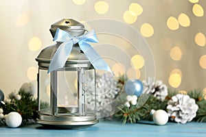 Christmas lantern with burning candle and festive decor on light blue wooden table against blurred lights
