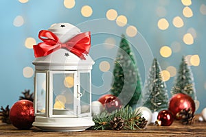 Christmas lantern with burning candle and festive ornaments on wooden table against blurred lights. Space for text