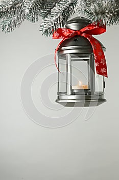 Christmas lantern with candle hanging on snowy fir tree branch against light background. Space for text