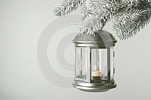 Christmas lantern with candle hanging on snowy fir tree branch against light background. Space for text