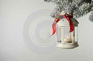 Christmas lantern with candle hanging on snowy fir tree branch against light background. Space for text