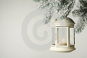 Christmas lantern with candle hanging on snowy fir tree branch against light background. Space for text