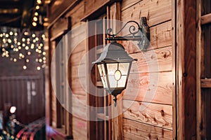 Christmas lantern. Festive illumination on a wooden house.