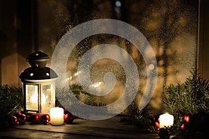 Christmas lantern with snowfall, candles, view from the window on the night street