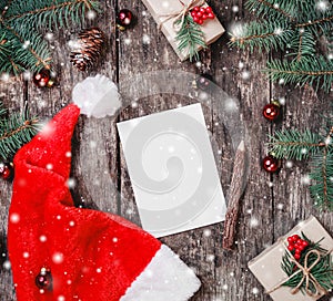 Christmas letter on wooden background with red Santa hat, Fir branches, pine cones, red decorations.