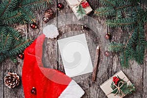Christmas letter on wooden background with red Santa hat, Fir branches, pine cones, red decorations