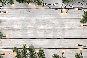 Christmas lights bulb and pine leaves decoration on white wood plank, frame border design.