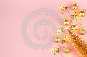 Christmas lights and decoration - golden stars garland glowing on soft light pastel pink background with christmas tree, balls.