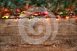 Christmas lights and fir tree branches on wooden background. New Year festive decorations with colorful glowing