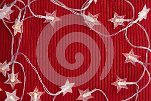 Christmas lights frame on red knitted background. Top view, flat lay, copy space