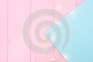 Christmas lights garland on blue paper border over pink wooden background. Scandinavian flat lay, copy space