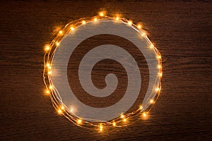 Christmas lights garland circular border over dark wooden background. Flat lay, copy space.