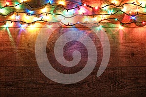 Christmas lights on wooden background. New Year festive decorations with colorful glowing Christmas lights. Colorful