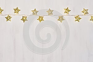 Christmas lights yellow stars burn on soft beige wooden background.