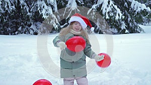 Christmas little girl in red santa claus hat. New Year's child in the forest with snow. Winter park and trees in the