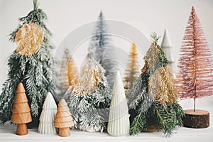 Christmas little trees and golden lights bokeh on white background. Winter magic forest, festive modern decor. Happy holidays.