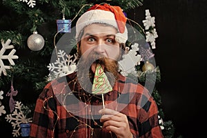 Christmas man with beard on happy face lick lollipop candy