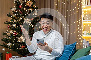 Christmas man near tree at home reading good news from phone got win and discount in online casino, Asian man holding