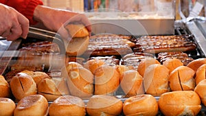 Christmas market, national German sausages are grilled, next to buns. Women`s hands turn Nuremberg sausages with help of