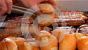 Christmas market, national German sausages are grilled, next to buns. Women`s hands turn Nuremberg sausages with help of