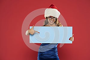 Christmas, x-mas, people, advertisement, sale concept - happy woman in blue dress and santa helper hat with blank blue board on a