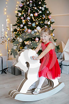 Christmas,x-mas,winter concept - girl in red dress sitting on wood horse toy in New Year& x27;s decorations