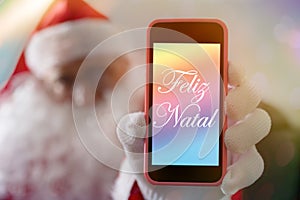 Christmas message in portuguese: Feliz Natal from Santa Claus or Saint Nicholas showing cell phone screen. Blurred background