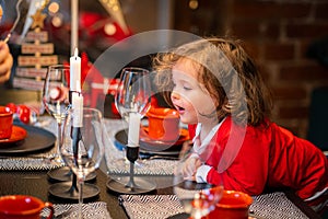 Christmas miracle, happiness, little curly girl blows out candle on table decorated with New Year decorations at home