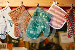 Christmas mittens potholders hang in kitchen against the background of blurry kitchen appliances.