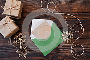 Christmas mockup holiday letter Blank paper in green envelope with wooden snowflakes and gift boxes on wood table, with space for