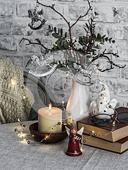 Christmas mood still life. Burning candle,stack of books, christmas tree, garland, knitting plaid on the table