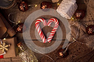 Christmas mood still life on a wooden background with heart-shaped candy cane, Happy holidays gift box, candles and lights, xmas b