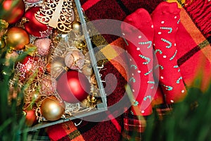 Christmas mood: wooden box with Xmas decoration of warm colors and feet in red socks with candy canes on checkered plaid