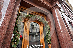 Christmas morning. House with a decorated door with a Christmas wreath and tree branches. Street european city.