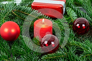 Christmas motif with red burning candle surrounded by Nordmann fir branches, red christmas tree balls and gift parcel