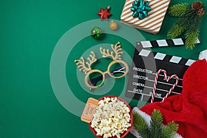 Christmas movie night and party concept with popcorn, Santa hat, decorations and movie clapper board on green background. Top