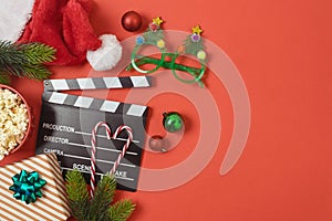 Christmas movie night and party concept with popcorn, santa hat, decorations and movie clapper board on red background. Top view