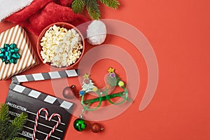 Christmas movie night and party concept with popcorn, santa hat, decorations and movie clapper board on red background. Top view