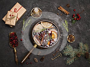 Christmas mulled red wine with the addition of spices and citrus fruits in a small vintage copper pan on a black background and