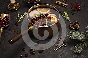 Christmas mulled red wine with the addition of spices and citrus fruits in a small vintage copper pan on a black background, side