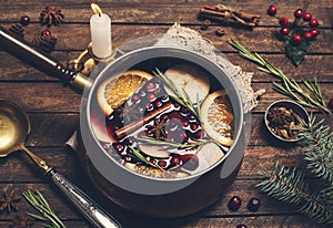 Christmas mulled red wine with the addition of spices and citrus fruits in a small vintage copper pan on a rustic wooden table,