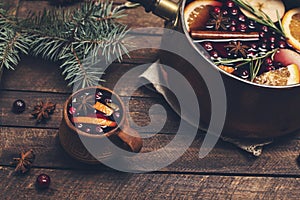 Christmas mulled red wine with the addition of spices and citrus fruits in a small vintage copper pan on a rustic wooden table,