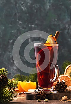 Christmas mulled red wine with spices and fruits in tall glass on wooden rustic table. Traditional Christmas or NewYear warming