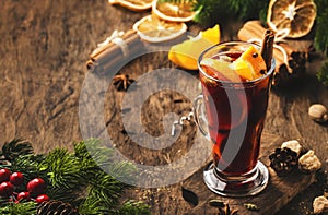 Christmas mulled red wine with spices and fruits in tall glass on wooden rustic table. Traditional Christmas or NewYear warming